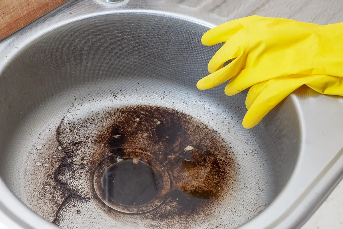 Kitchen sink backing up with standing water in Gaffney, with dirty water around the drain and yellow cleaning gloves nearby.