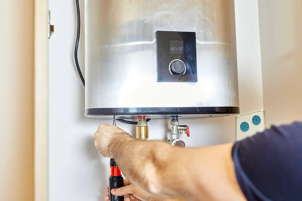 Technician inspecting connections beneath a tank water heater for a gas vs electric water heater comparison.