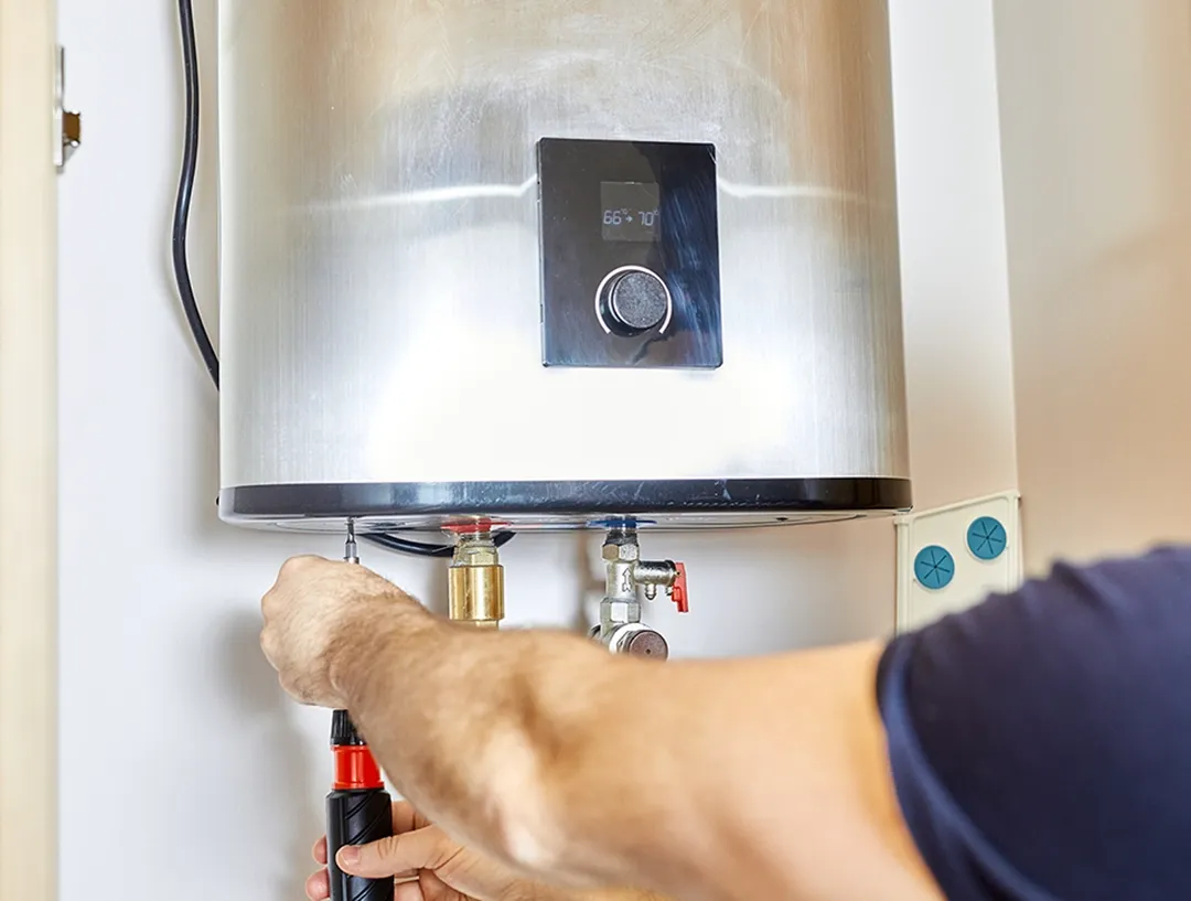 Technician inspecting connections beneath a water heater leaking from bottom components.