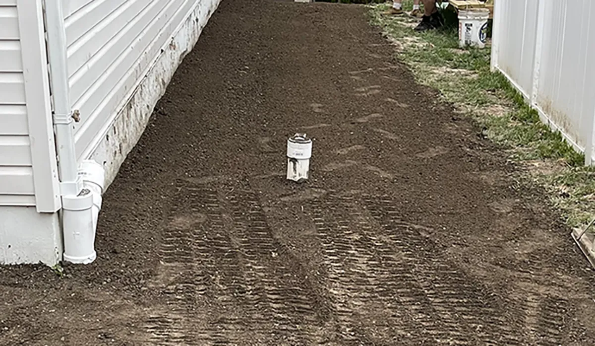 Sewer cleanout: a newly installed white plumbing fixture or meter positioned in a freshly prepared dirt area alongside