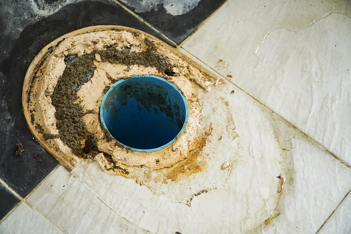 Exposed toilet drain and damaged floor flange before offset toilet flange replacement.