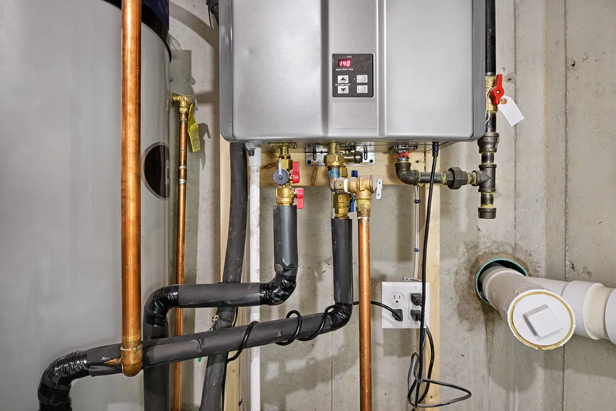 Tankless vs traditional water heater pros and cons: wall-mounted tankless water heater installed beside a traditional tank