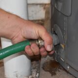 man attaching a garden hose to the water heater to drain it